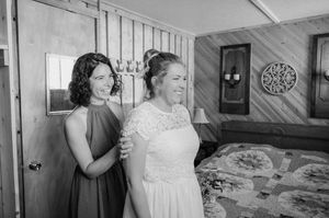 A black and white photograph showing two women in a room, one wearing a white lace dress and the other in a dark dress.
