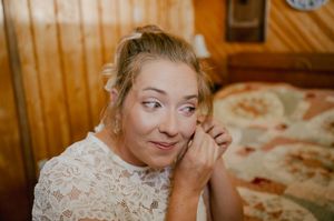 A person in a white lace top smiles warmly while looking to the side in a wood-paneled room.