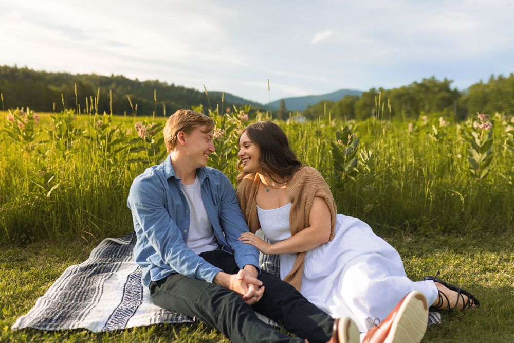 Couple enjoying a romantic picnic on a blanket in a sunny meadow filled with yellow wildflowers at sunset.