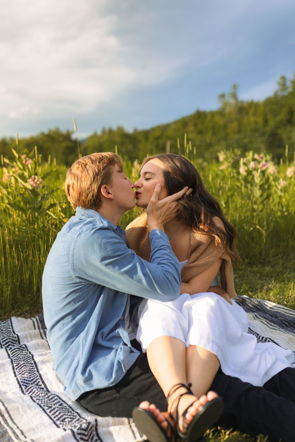Romantic young couple sharing a tender moment on a blanket in a sunny meadow with mountains in the background.
