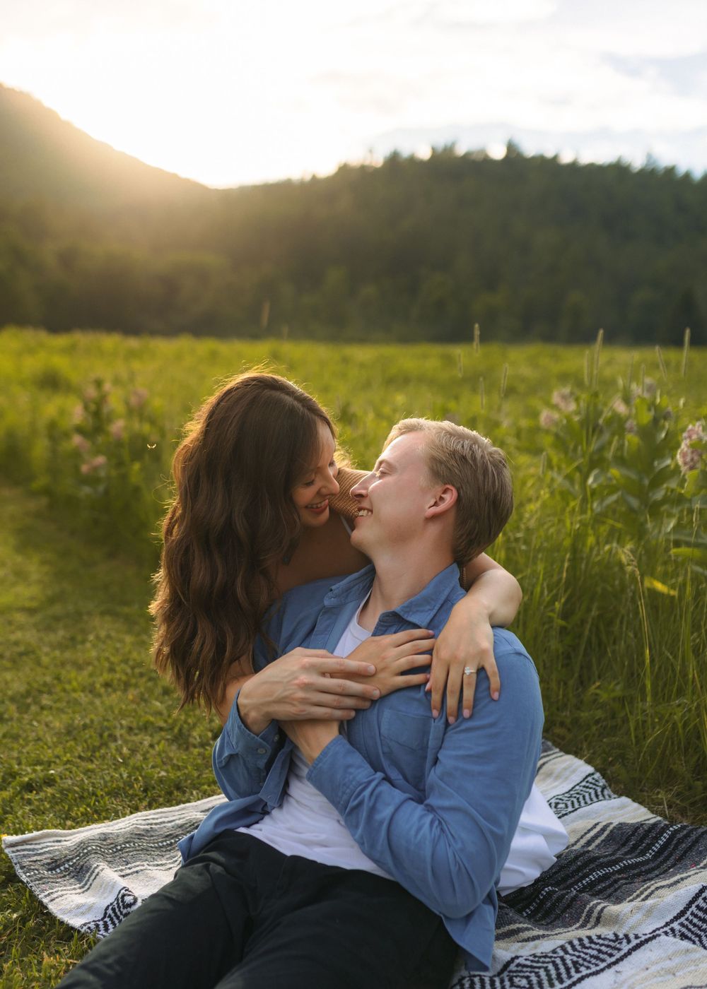 A couple shares romantic moments while lounging on a blanket in a sunny meadow.