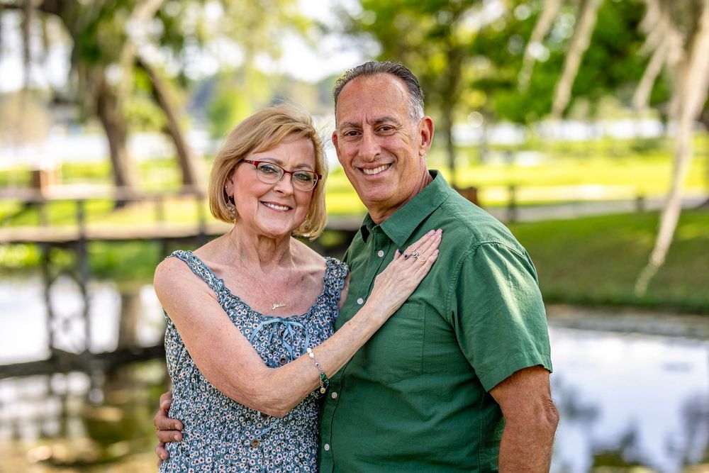 Outdoor couple photos in green natural setting with water and palm trees in background.