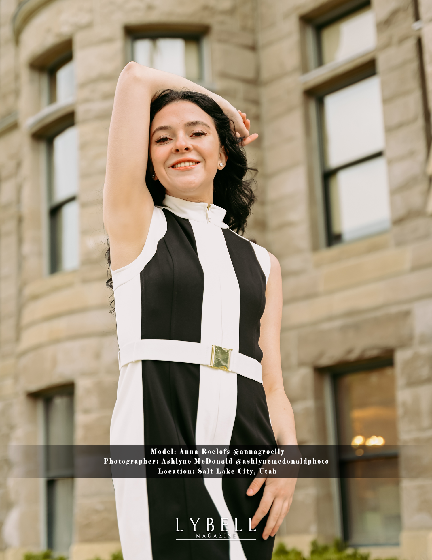 A fashionable black and white sleeveless dress with a belt photographed in front of a stone building.