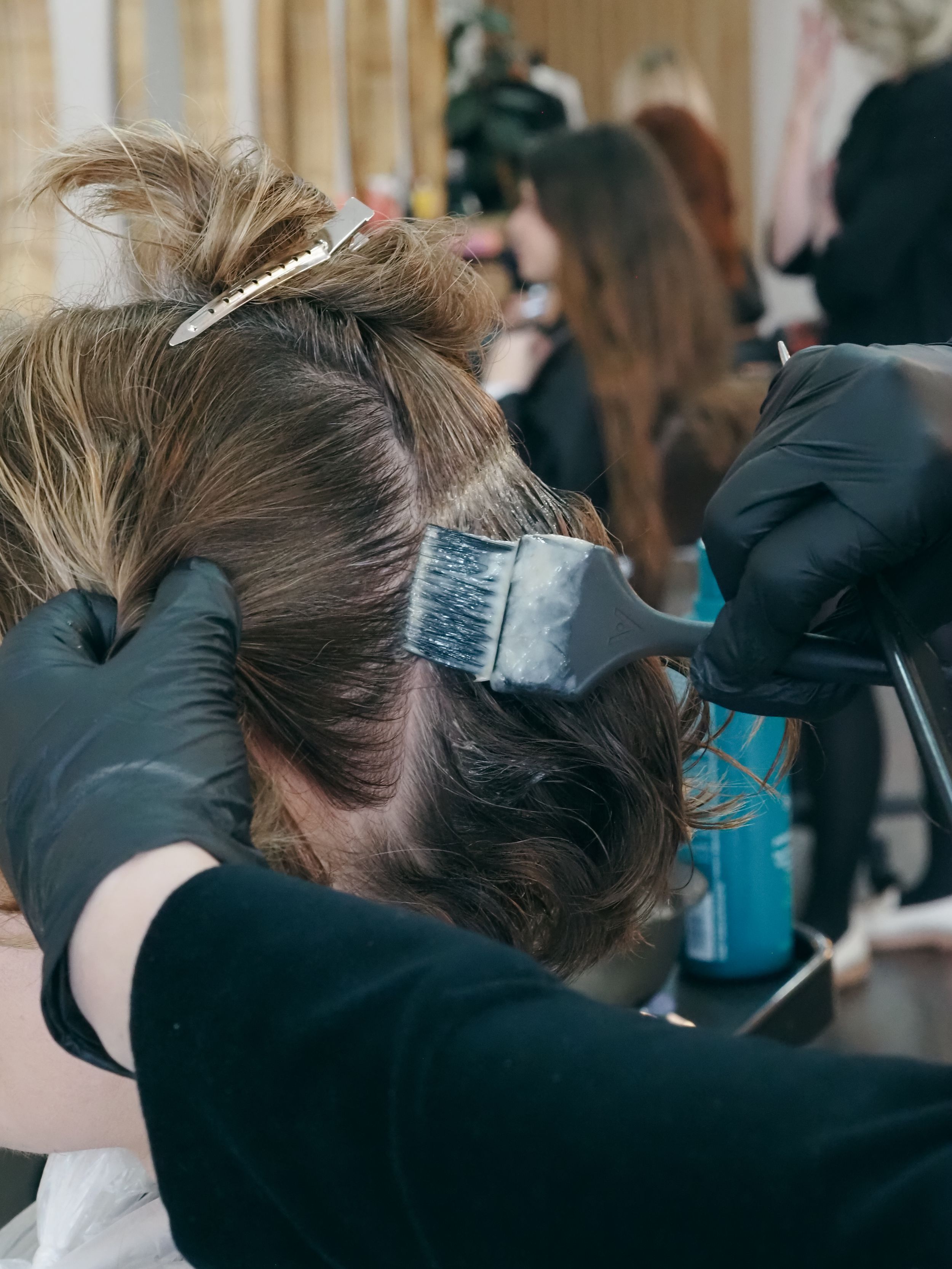 Close-up of hairdresser applying hair dye with brush in professional salon setting.