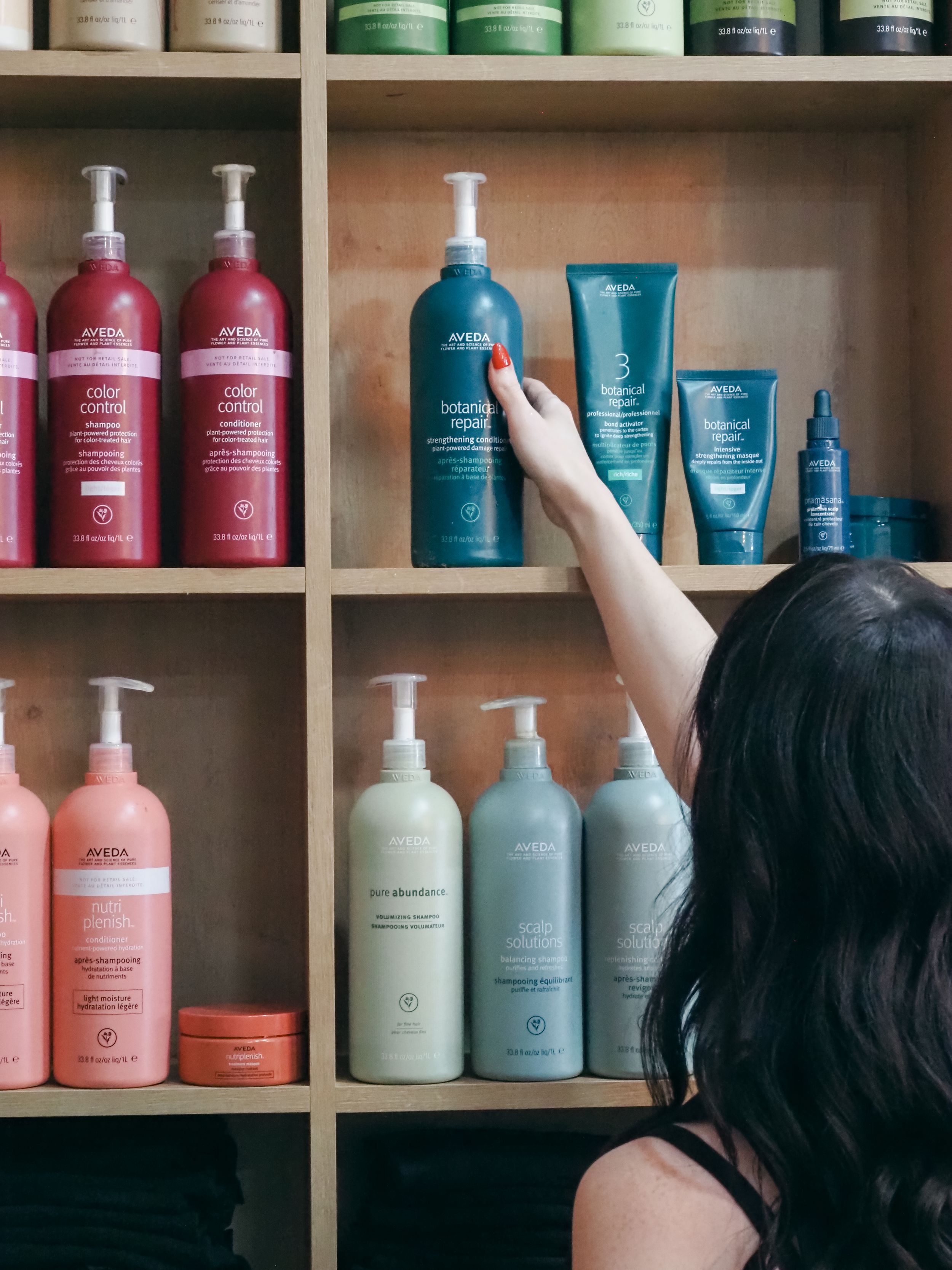 Colorful hair care products arranged on wooden shelves with pink, blue and white bottles in a salon setting.