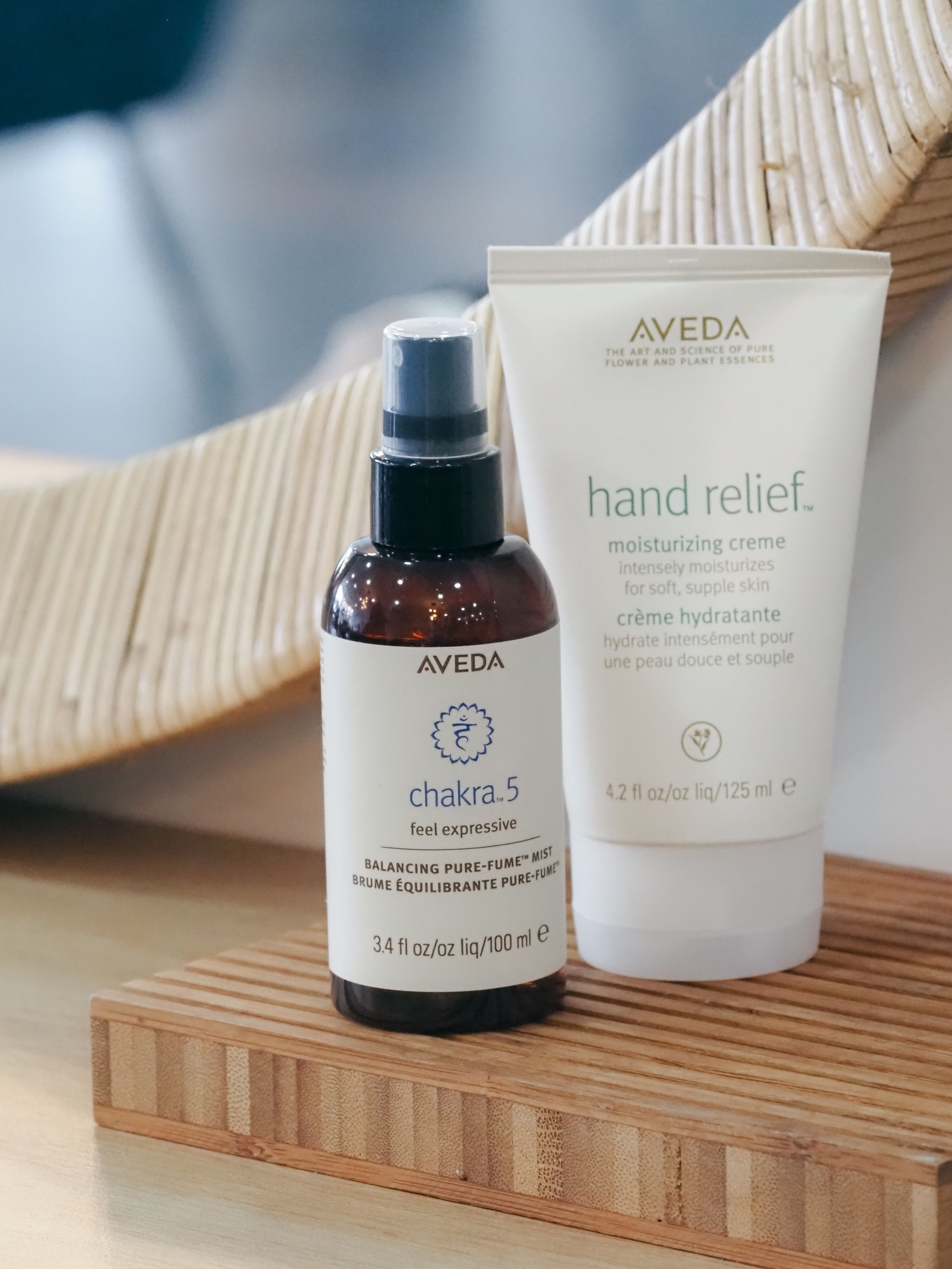 Two Aveda beauty products including hand relief moisturizing creme and chakra spray displayed on wooden surface.
