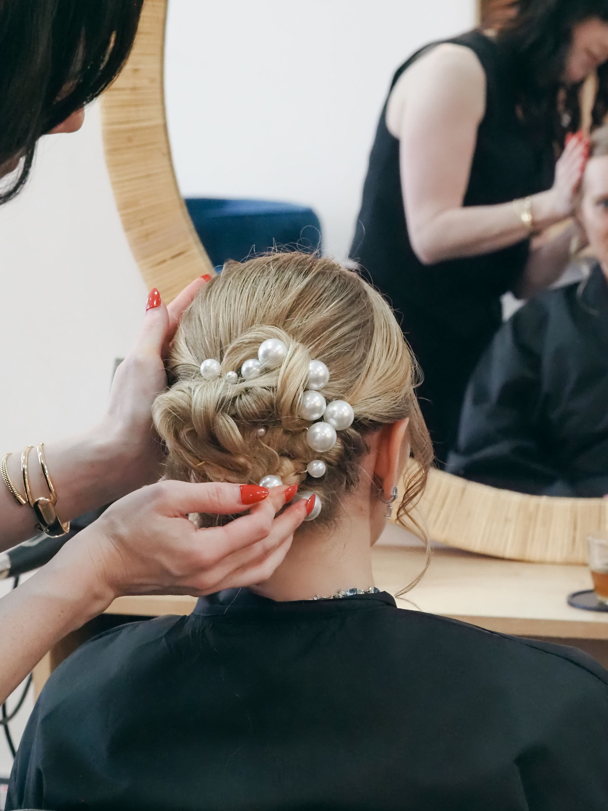 A delicate bridal hairstyle being styled with white flower and pearl hair accessories in a salon setting.