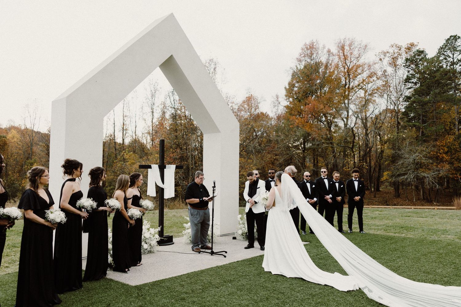 Wedding party in formal attire poses on grass beneath weeping willow trees for outdoor bridal portraits.