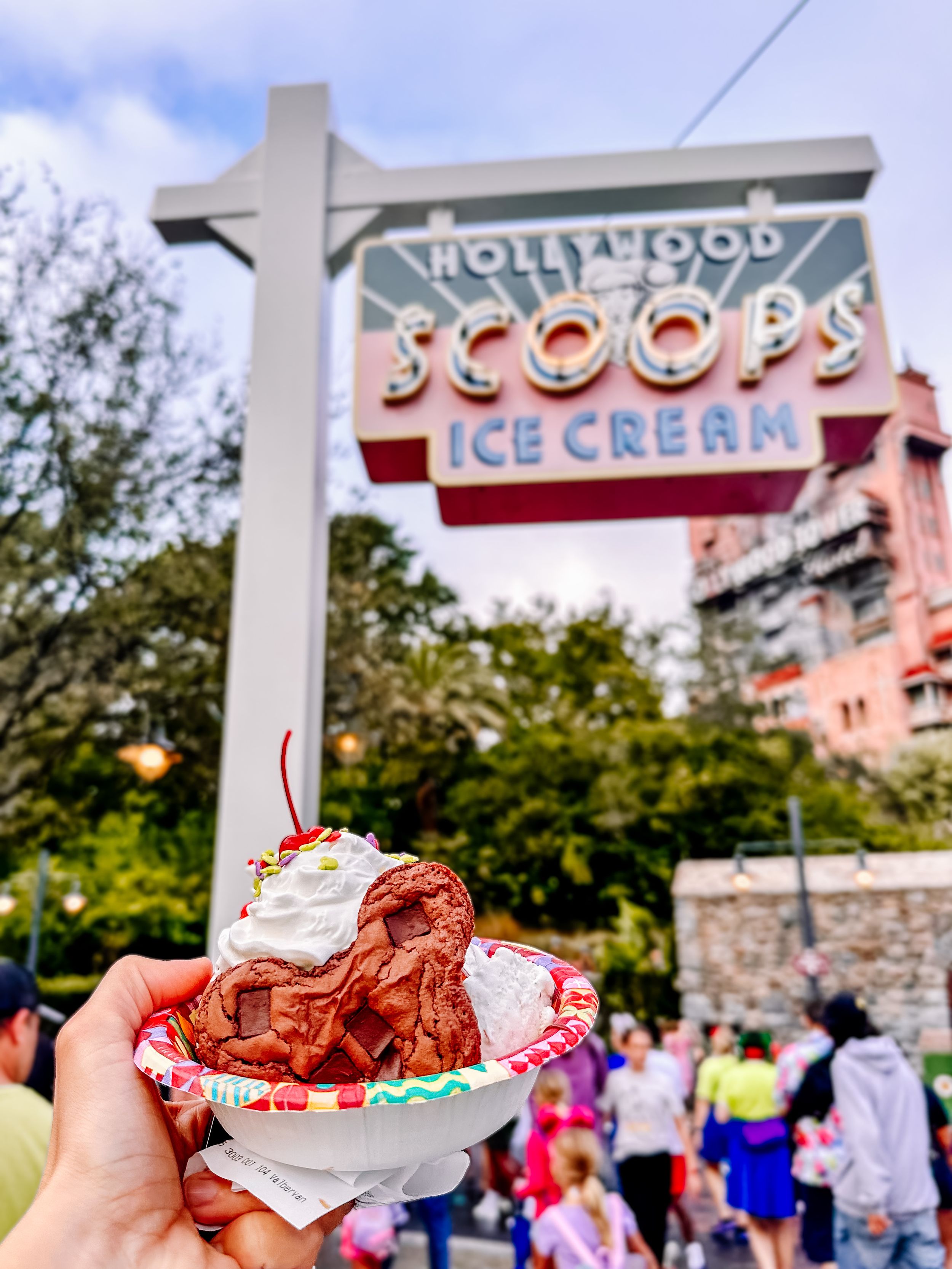 Ice cream sundae held up in front of the Hollywood Scoops storefront sign.