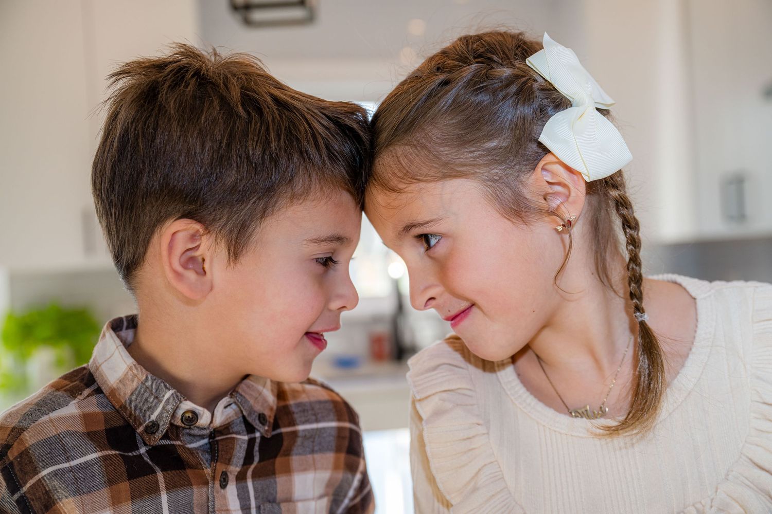 Two young people share a playful moment in a kitchen setting, leaning close together with a white bow accessory.