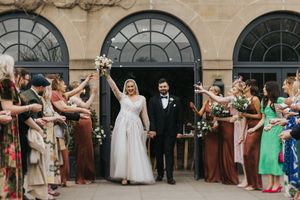 A joyous wedding celebration with guests tossing confetti as the newlyweds exit through stone archways.