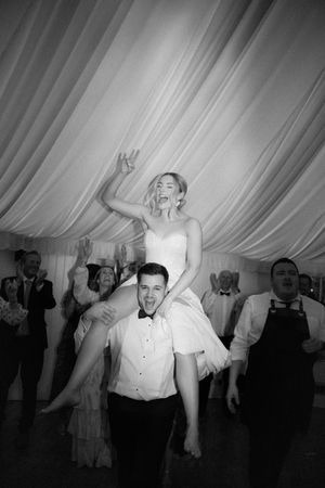 A joyful bride being carried on the shoulders of her dance partner during a wedding reception.