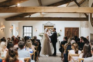 People gather in a rustic wedding venue with exposed wooden beams and white walls during a celebratory event.