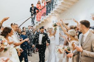 Wedding guests shower a happy couple descending a staircase with confetti during a joyful celebration exit.