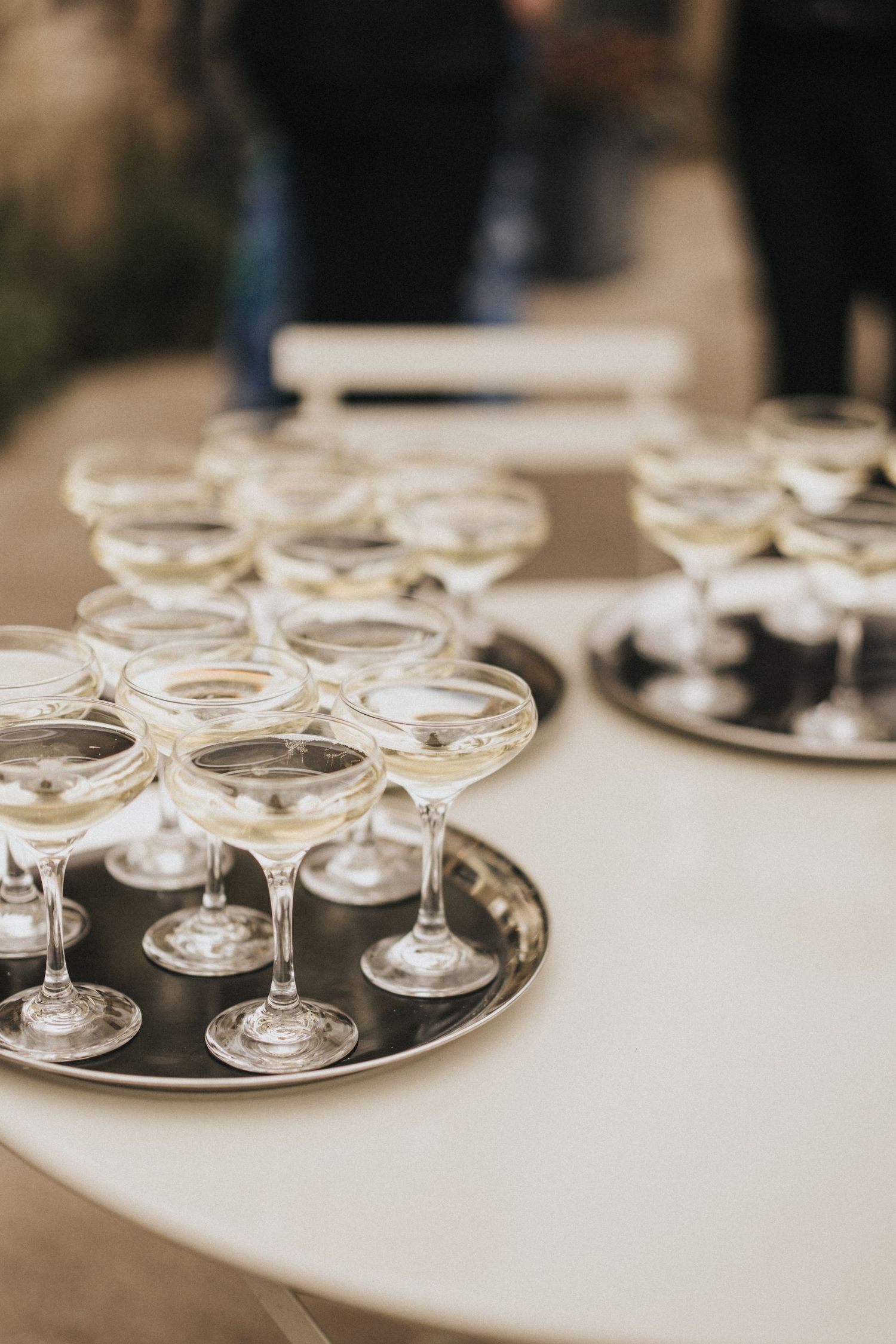 Elegant champagne coupe glasses arranged on silver serving trays at an upscale event.