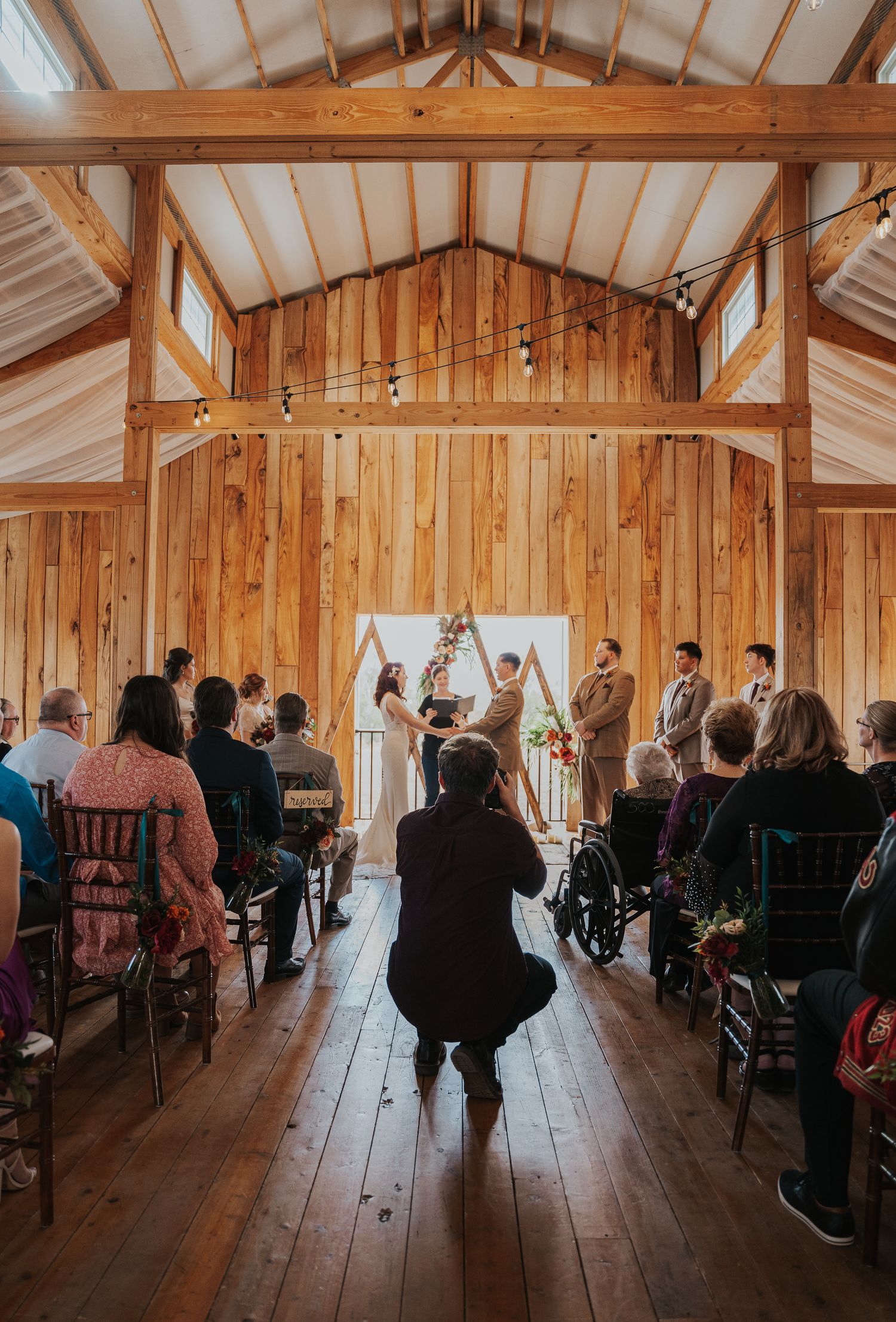 photographer capturing photo of wedding ceremony in a warmly lit venue with bride and groom at the altar