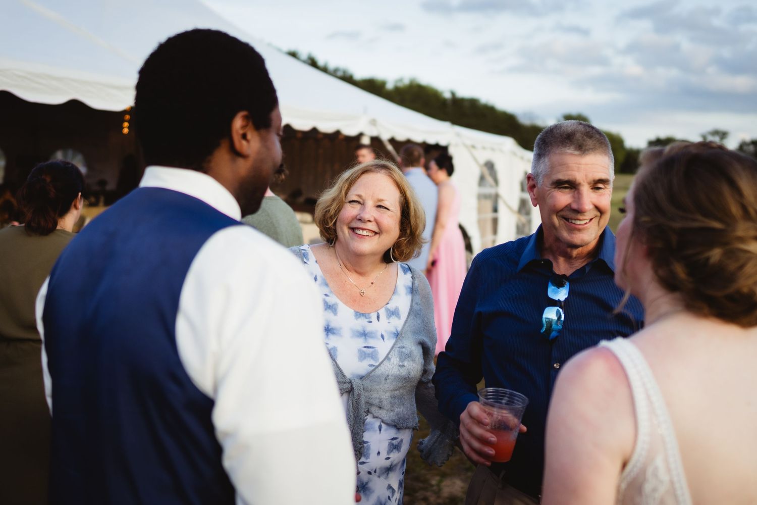 A group of guests socializing and laughing together at an outdoor event with a white tent in the background.