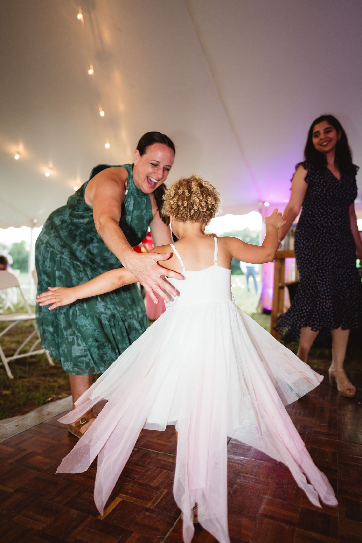 Reception guests dance together on a parquet dance floor under string lights at an evening wedding celebration.