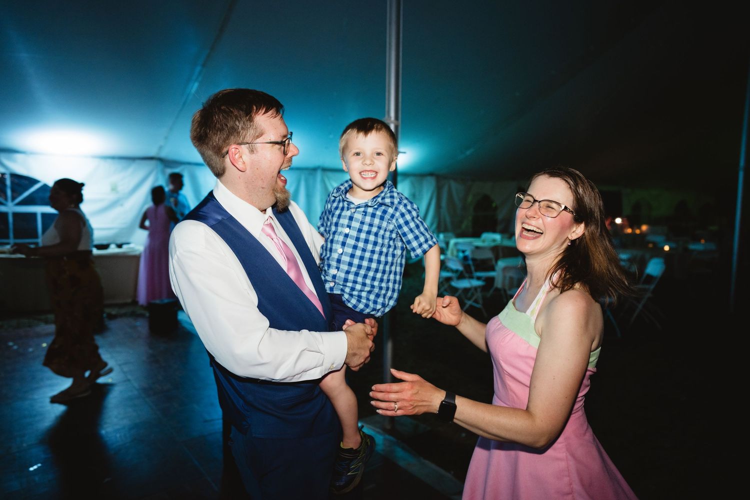Happy moment of dancing at an evening wedding reception under a blue-lit tent.