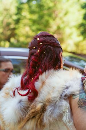 Vibrant red hair adorned with delicate flowers is styled against a fur shawl at an outdoor event.