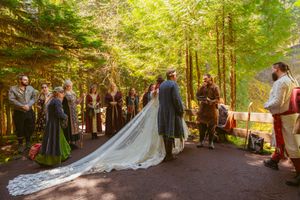 Forest wedding ceremony with guests and couple gathered among tall trees and natural scenery.