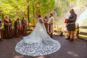 A forest wedding ceremony showing a stunning lace train on the bride's dress with guests in medieval attire.