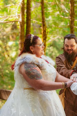 A joyful moment during a medieval-themed wedding ceremony in a forest setting.