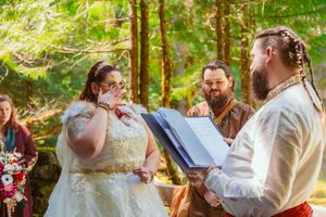 A joyful outdoor wedding ceremony in a forest with a couple and officiant.