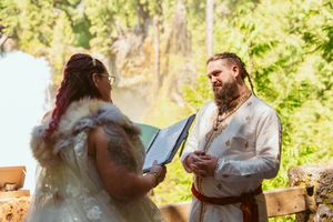 Wedding ceremony participants in medieval-inspired attire gather in a wooded outdoor setting.