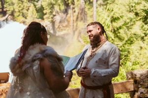 Intimate forest wedding ceremony with attendees in traditional dress beneath sunlit trees.