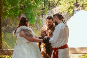 A medieval-themed wedding ceremony takes place outdoors with participants wearing traditional garments by a waterfall.