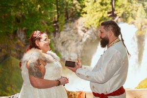 A couple exchanges rings during their medieval-themed outdoor wedding ceremony with a waterfall backdrop.
