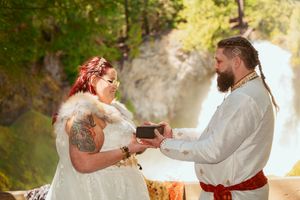 A couple exchanges rings during an outdoor waterfall wedding ceremony in rustic bohemian attire.
