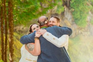 Three people share an emotional embrace during an outdoor forest wedding ceremony.