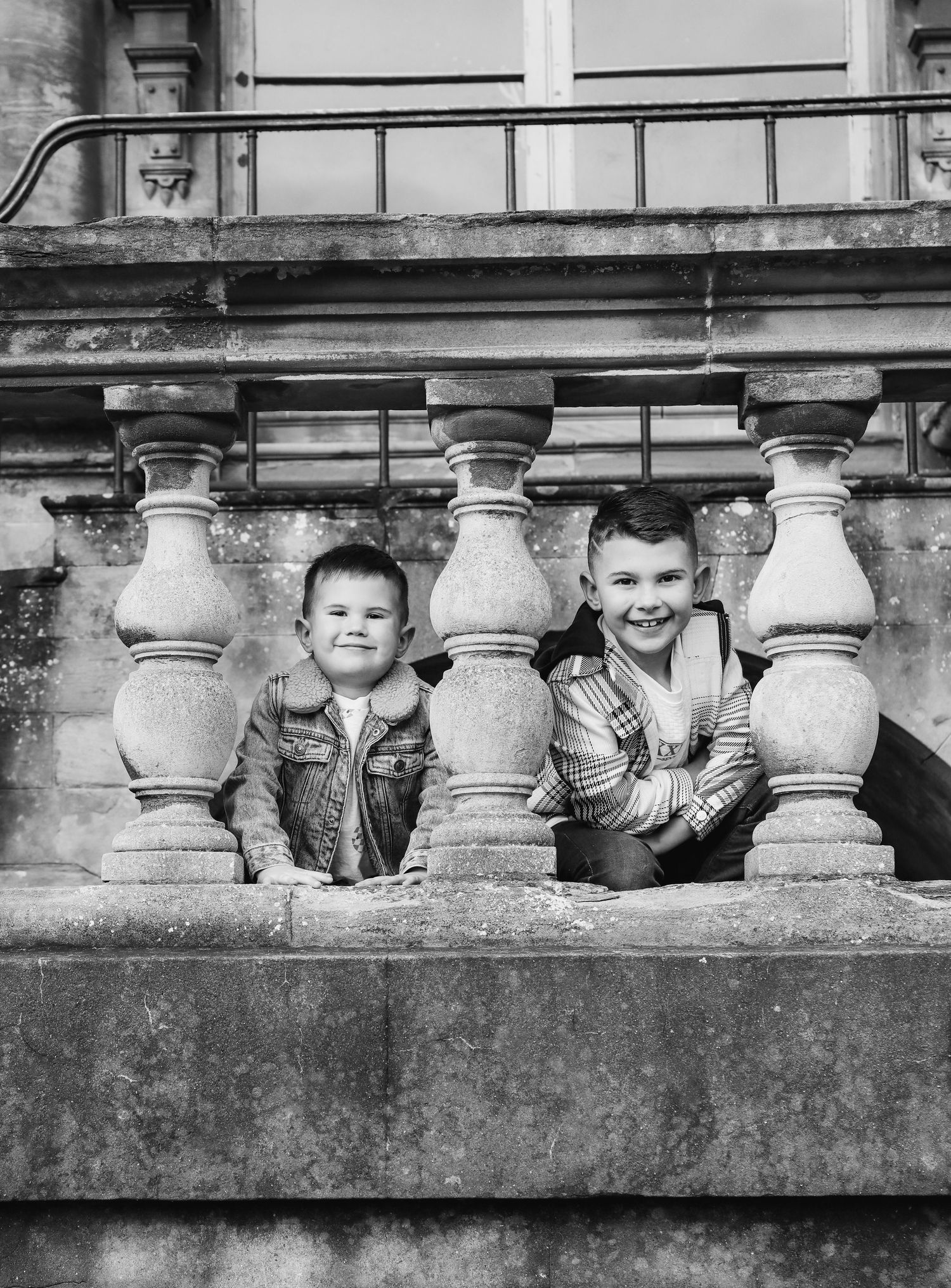 A black and white photograph shows two brothers peeking through stone balusters during family shoot in Nottingham