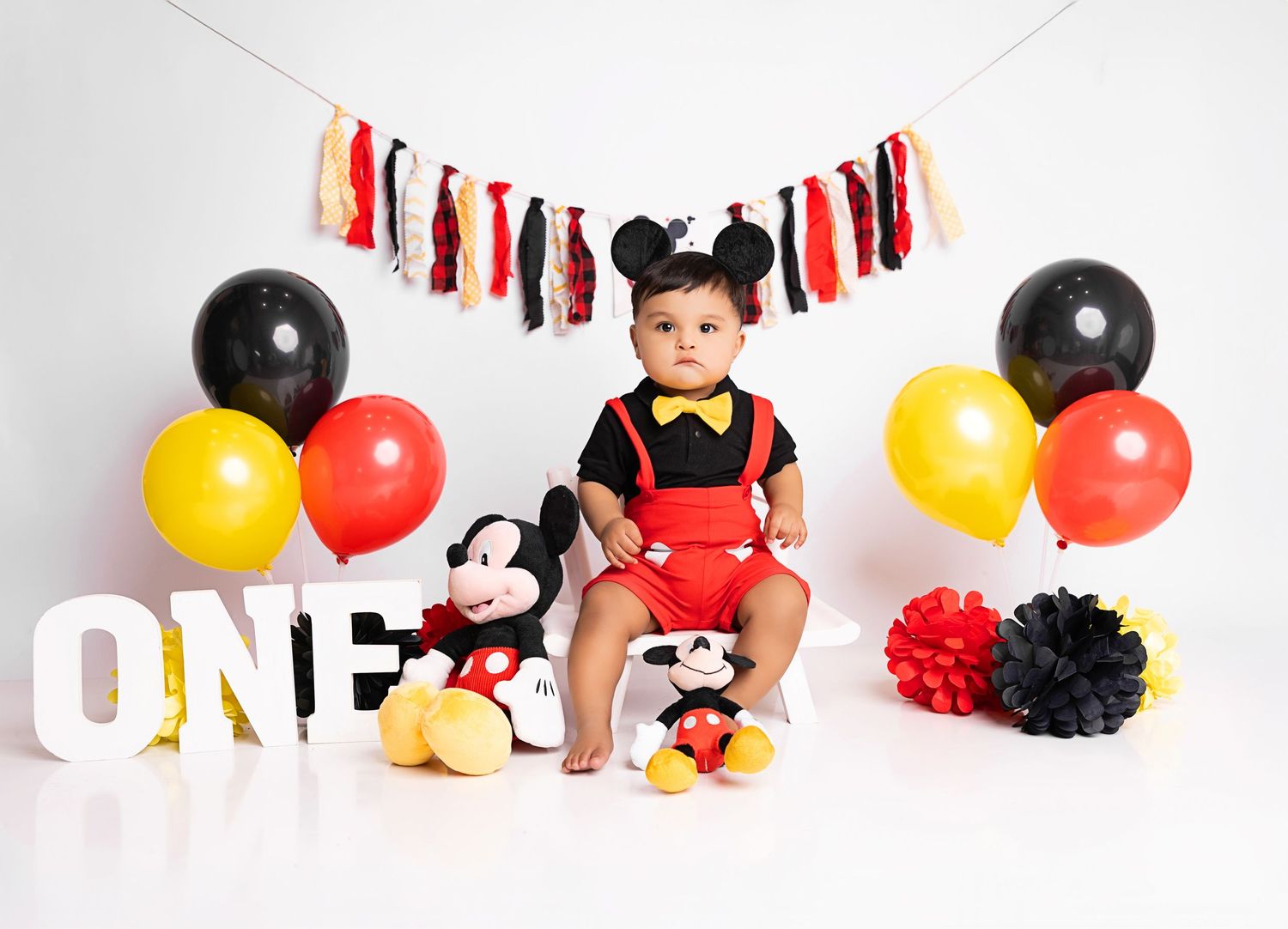 A festive Mickey Mouse themed first birthday photo collage with red, yellow and black balloons and banners.