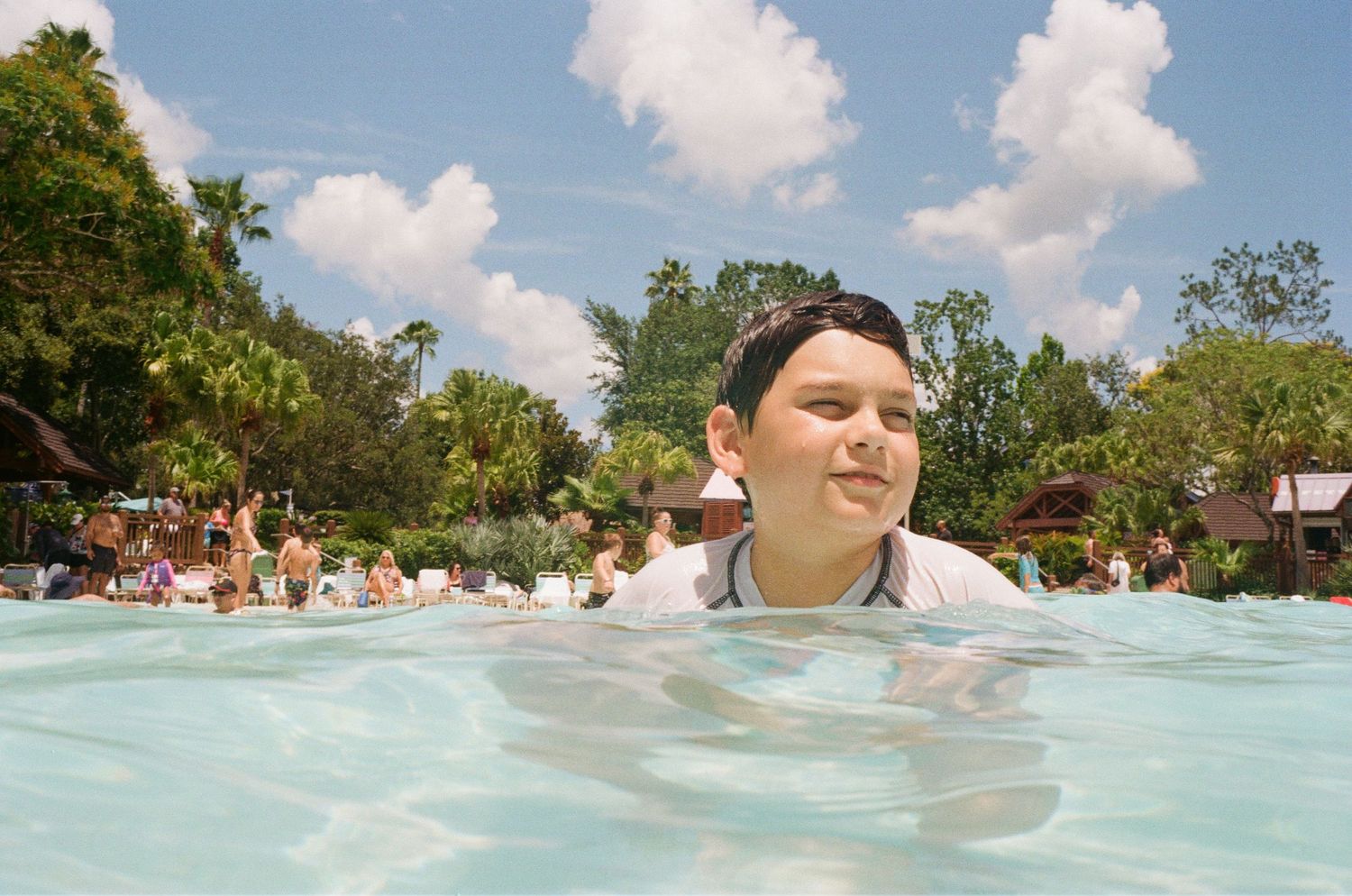 Someone enjoys a refreshing swim in a crowded outdoor pool on a sunny summer day with palm trees in the background.