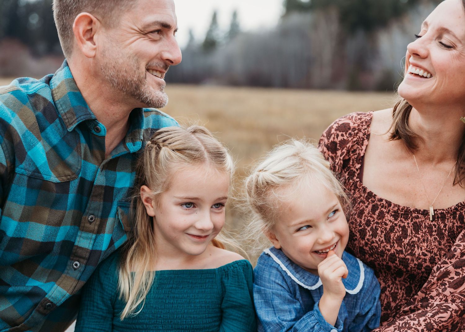 A happy family of four share joyful moments together during an outdoor autumn photoshoot.