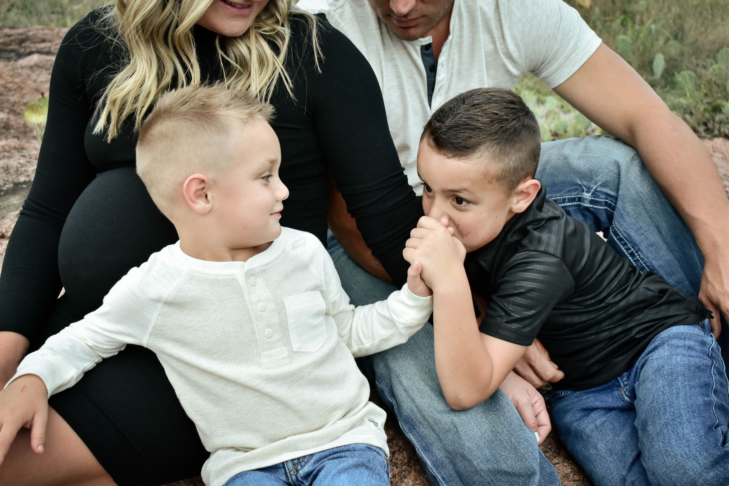 Family sits together on ground during casual outdoor portrait session.