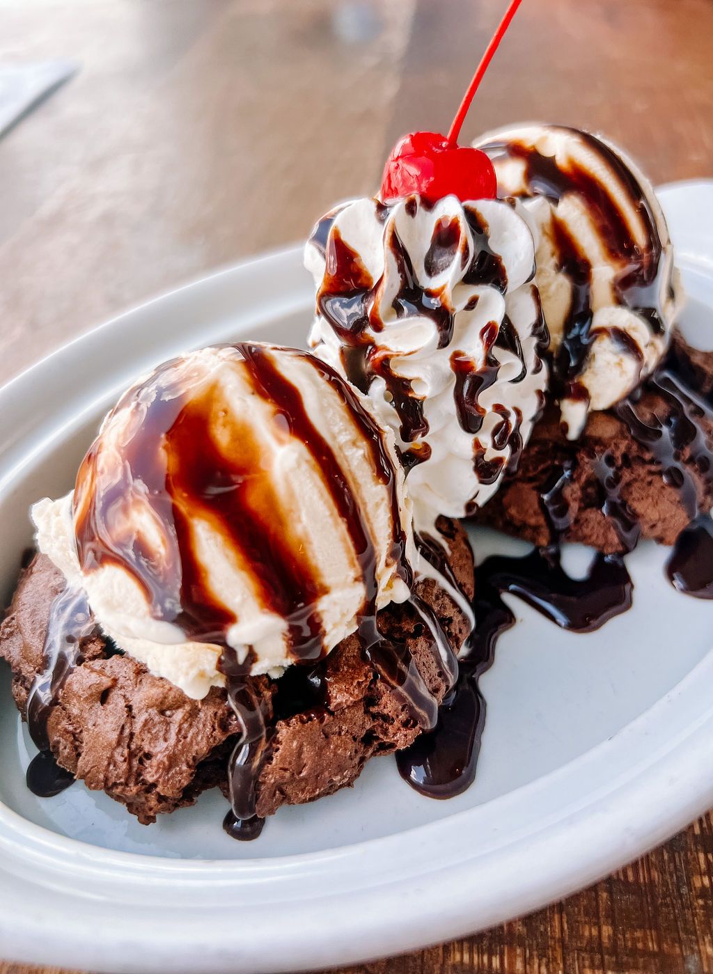 Chocolate ice cream sundae drizzled with chocolate sauce and topped with whipped cream and a cherry.
