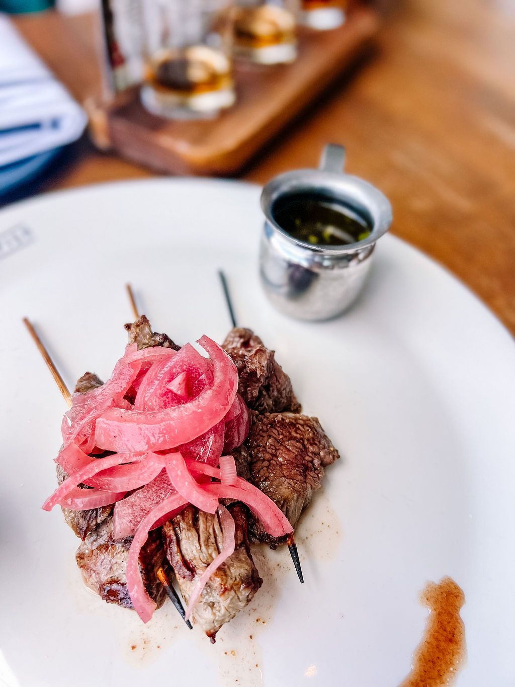 Grilled steak bites topped with pickled red onions served with a side of dipping sauce.