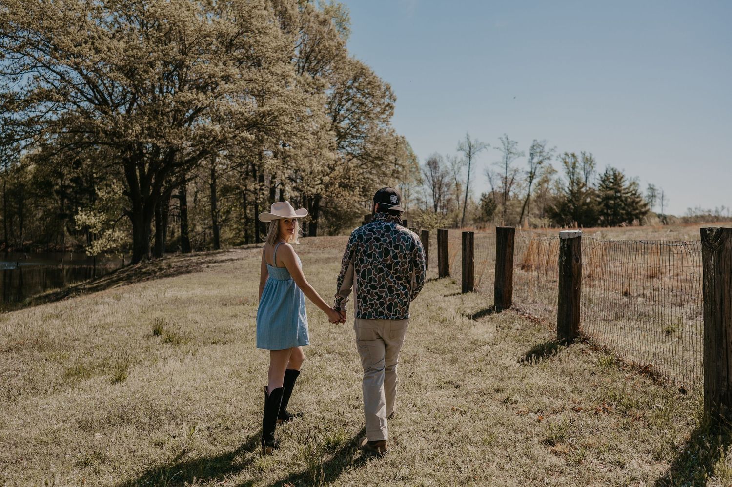 A couple strolls together through a golden autumn meadow on a hillside during a sunny afternoon.