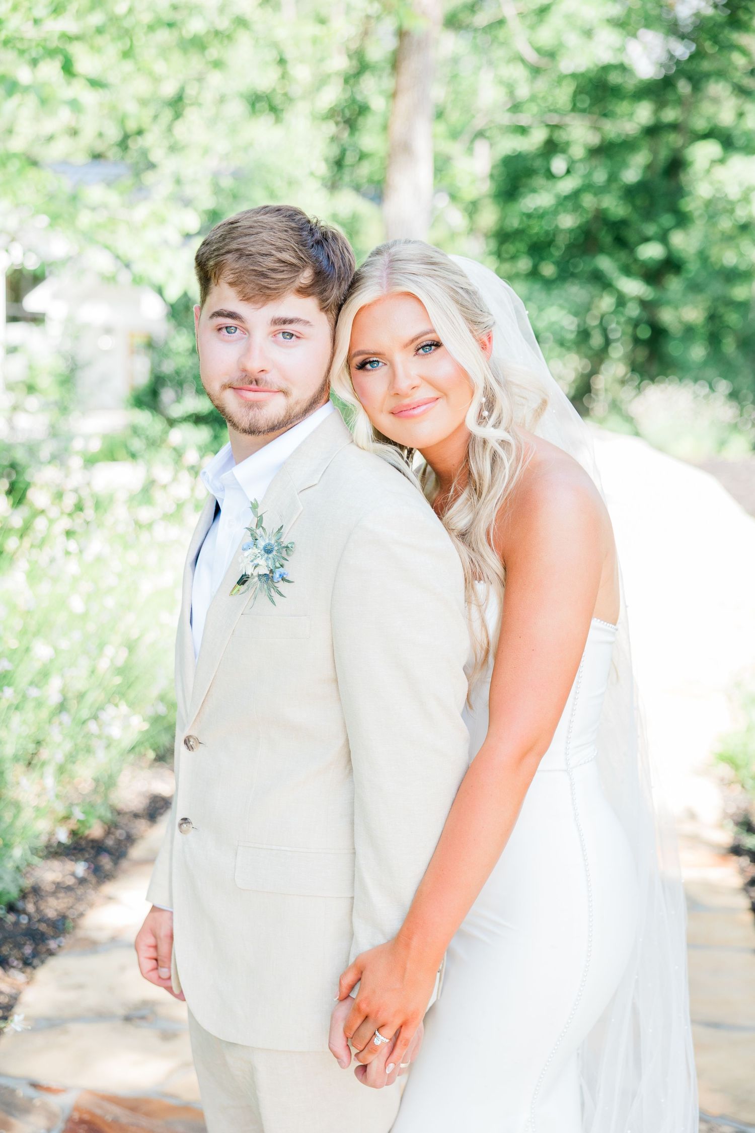 A romantic wedding moment captured under a flowing veil with a soft pastel blue boutonniere and light natural backdrop.