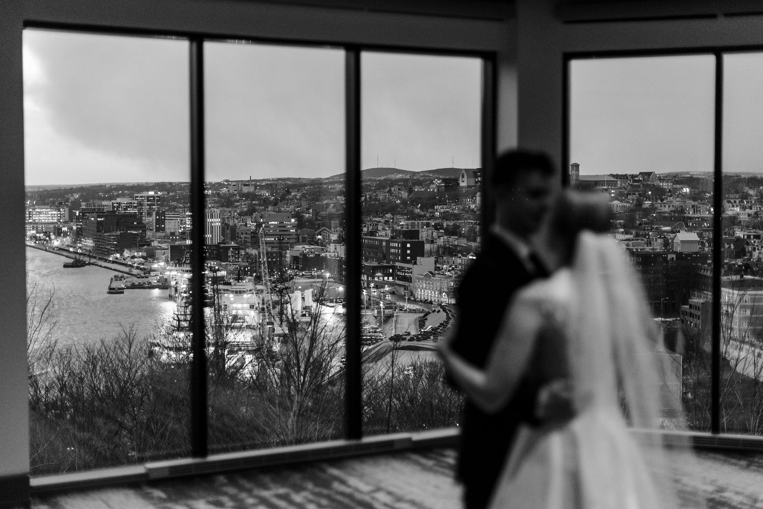 A black and white panoramic view shows silhouettes against large windows overlooking a cityscape.