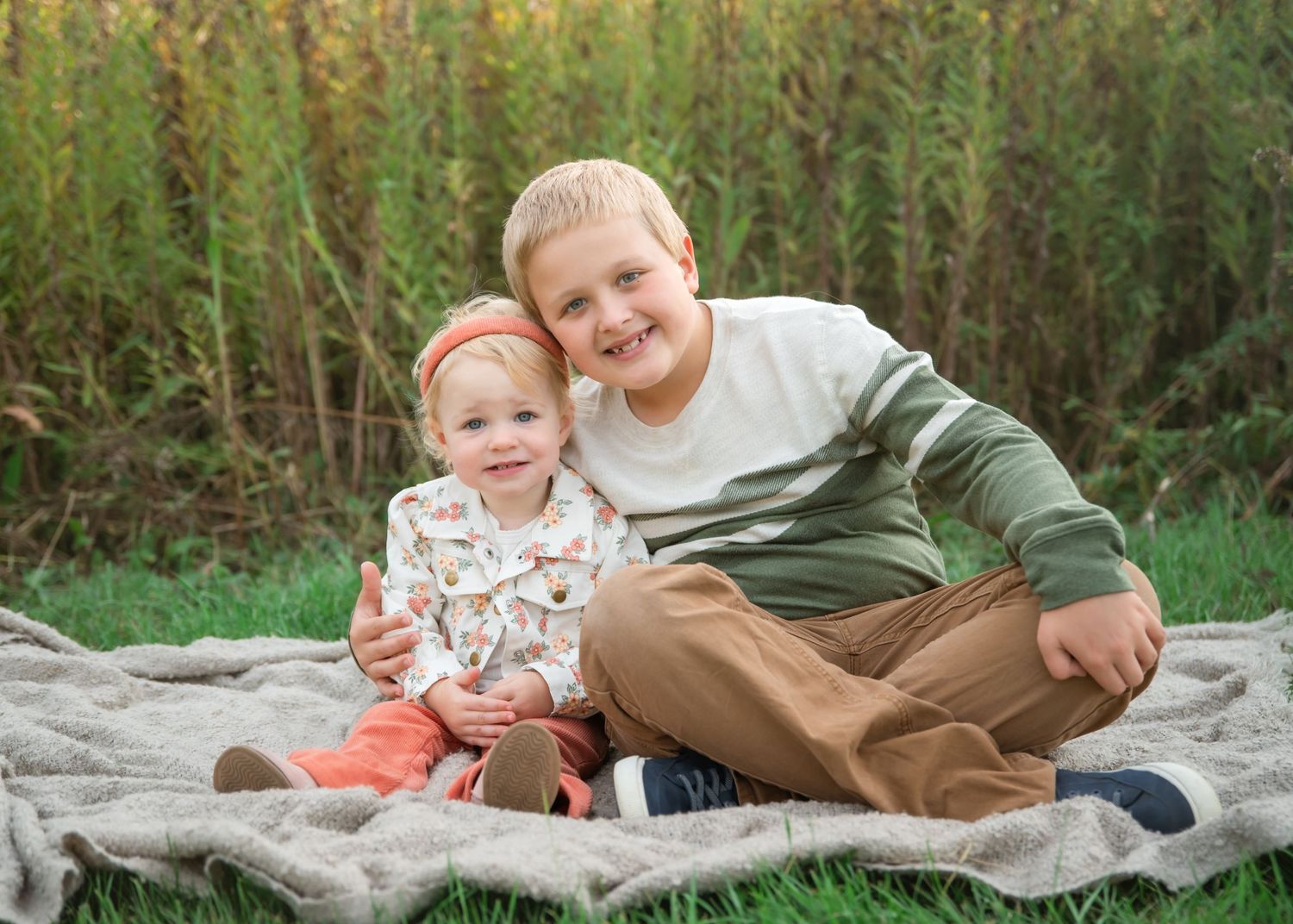 Children laying on a blanket in a grassy outdoor setting during a photo session.