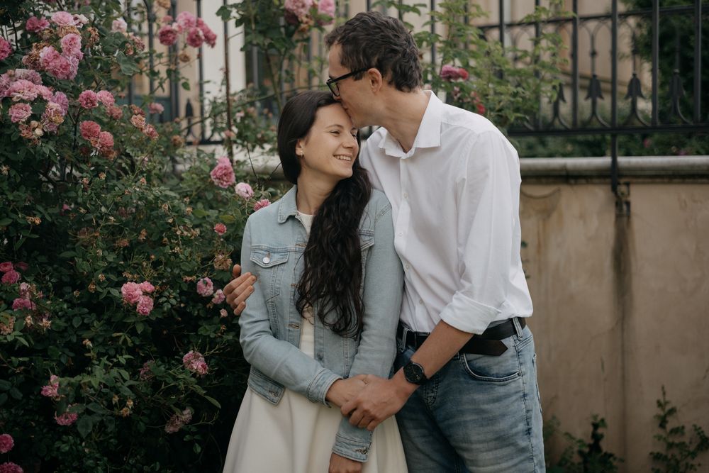 Romantic couple poses among blooming pink roses in a garden setting.