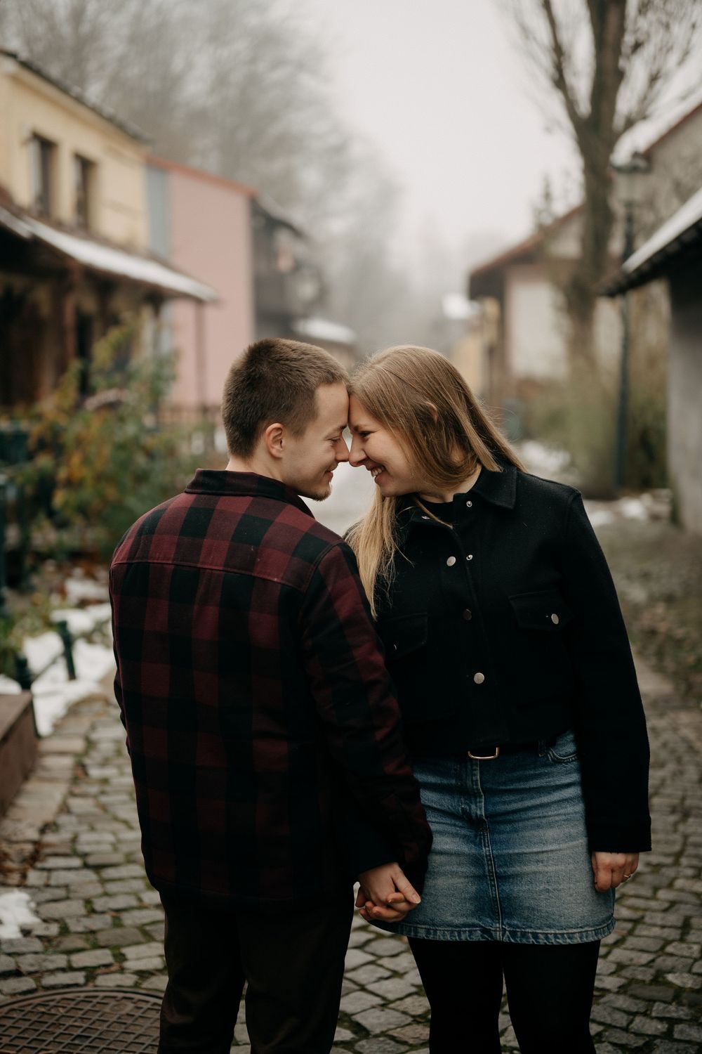 A couple in casual attire shares an intimate moment on a cobblestone street on a foggy day.