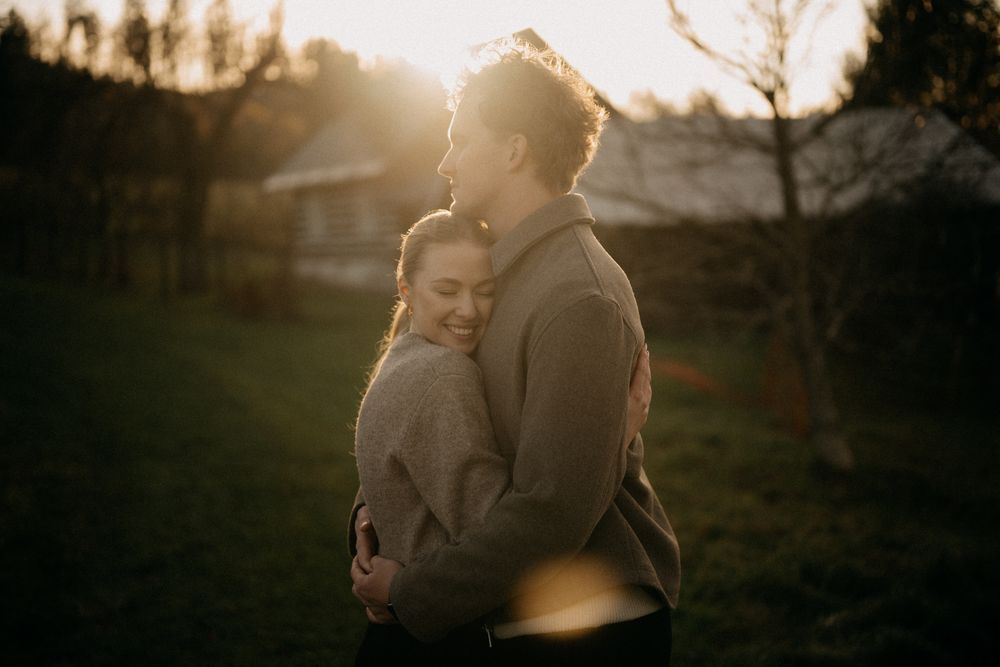 A romantic couple embraces in a golden sunset field with dramatic lighting and shadows.