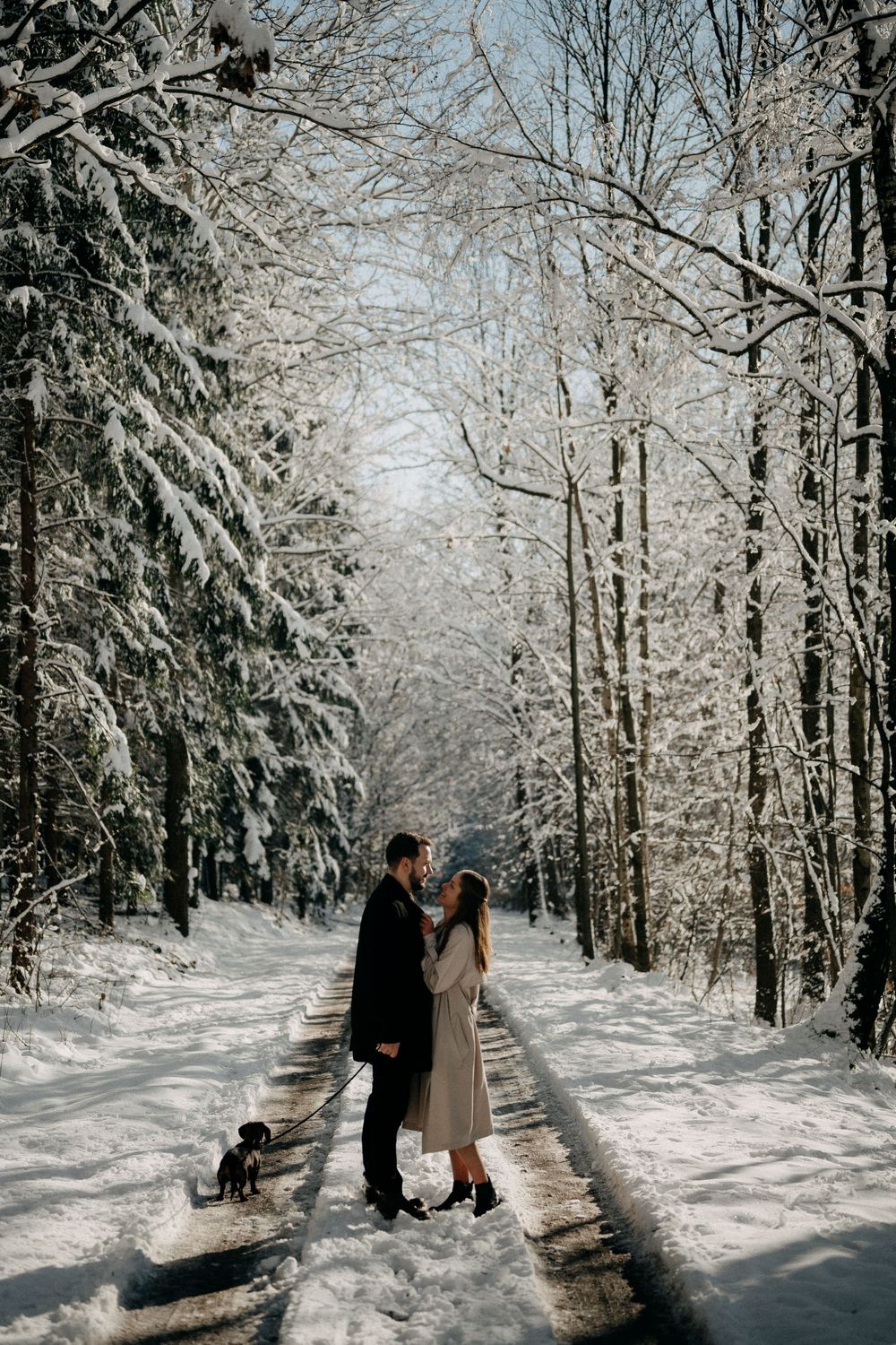 Couple shares tender moment on snowy forest path surrounded by frost-covered trees.