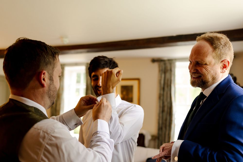 Groomsmen in navy suits and white shirts getting ready in a sunlit room.
